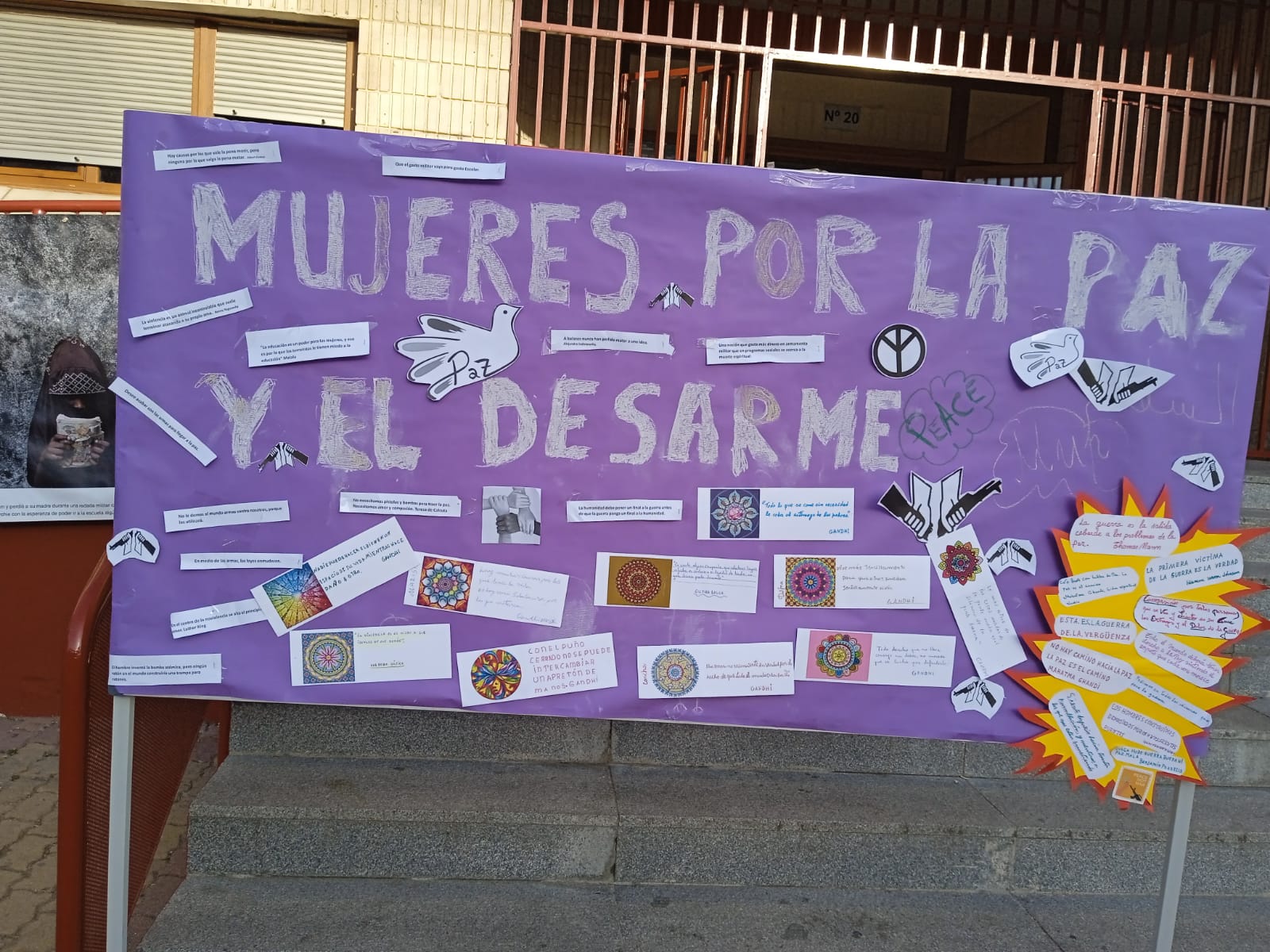 Pancarta en un panel en la calle. En ella está escrito "Mujeres por la paz y el desarme" y otros mensajes en letra más pequeña.