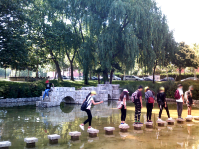 Grupo de personas encima de varias piedras en un estanque artificial, y al fondo los arcos de piedra que marcaban una de las entradas de mercancías a Valladolid