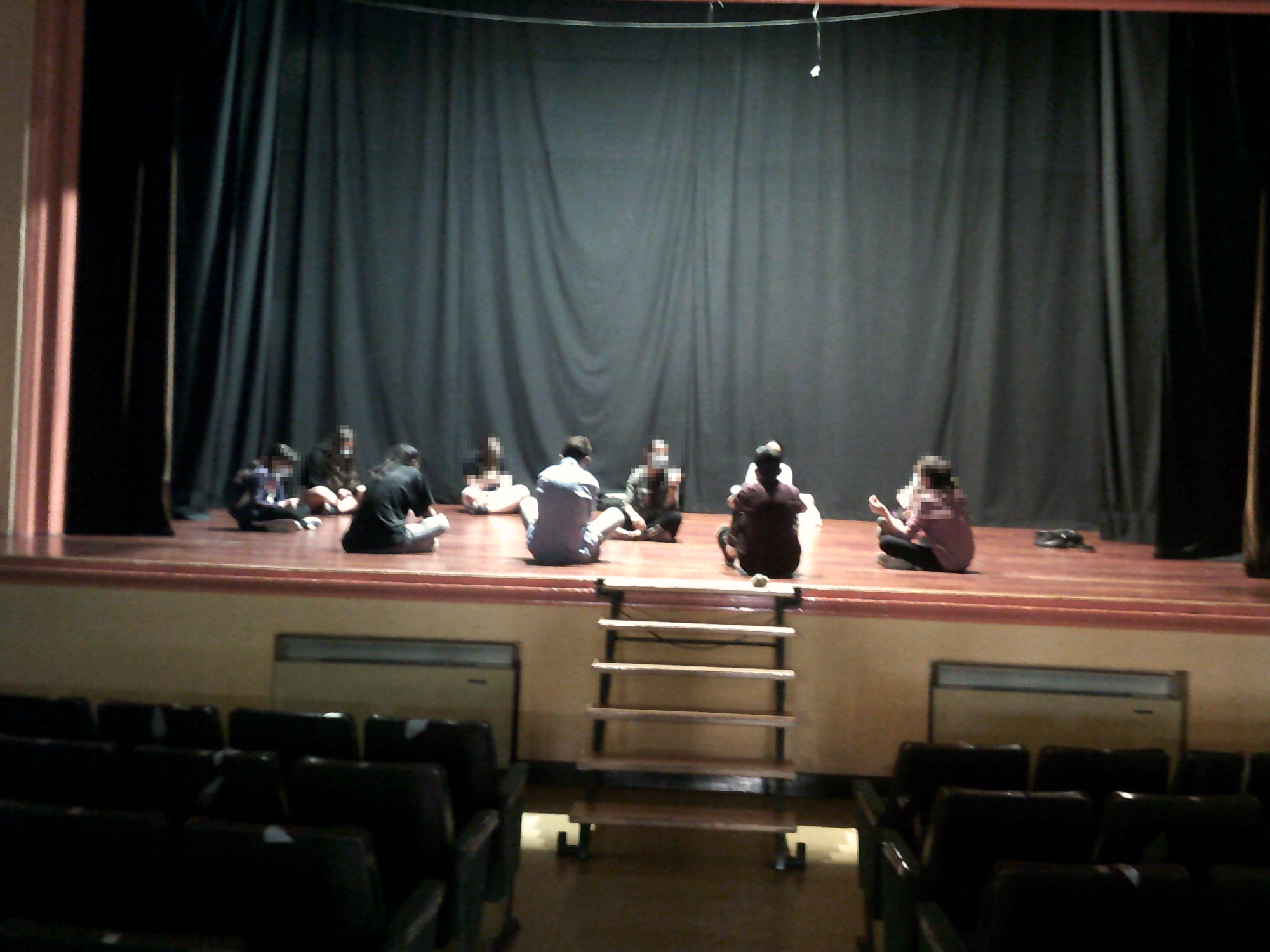 Personas sentadas en círculo en el escenario del teatro del CC Delicias